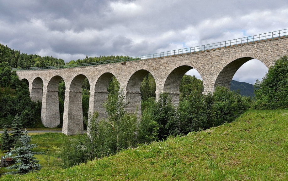 pohled na viadukt překleňující údolí, pod ním travnatý svah, pod ním vede silnice a na viaduktu je zelené zábradlí