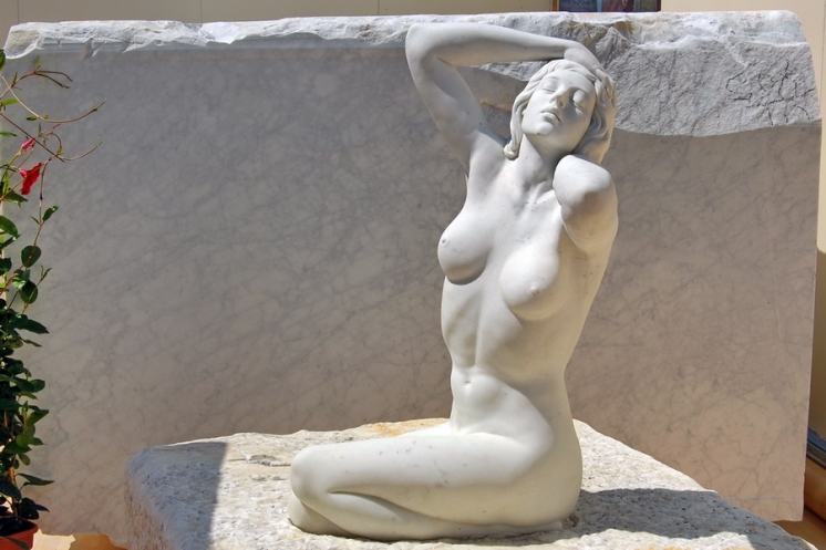 pohled na antickou dámskou sochu oslavující nahotu a lidskou přirozenost v póze držící se levou rukou za krk a pravou za vlasy v klečící pozici